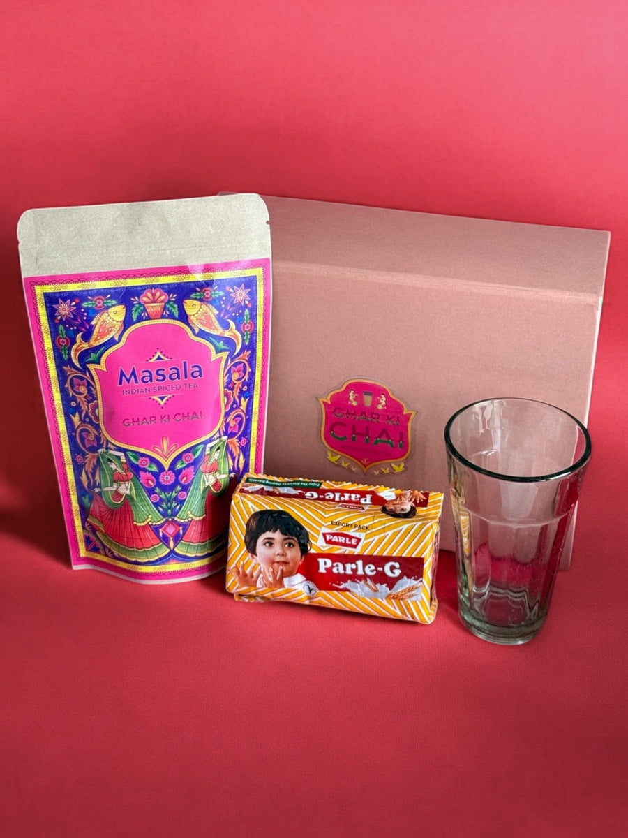 A Ghar Ki Chai Masala pouch, Parle-G biscuits and an empty chai glass arranged on a red product shoot background